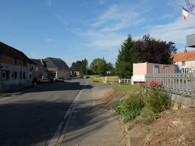 Vue de la Grand Rue de Sassegnies à côté du monument aux morts. Au fond, le clocher de l'église est visible.