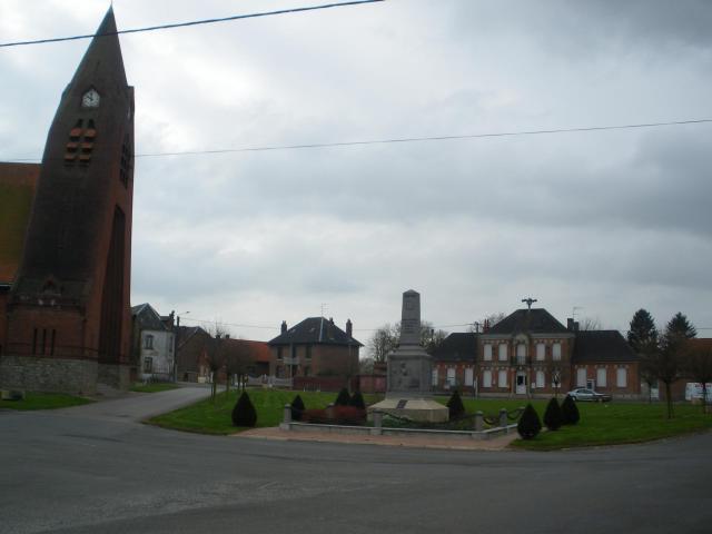 Vue de la place principale de Sauchy-Lestrée. De gauche à droite, l'église, le monument aux morts, la mairie.