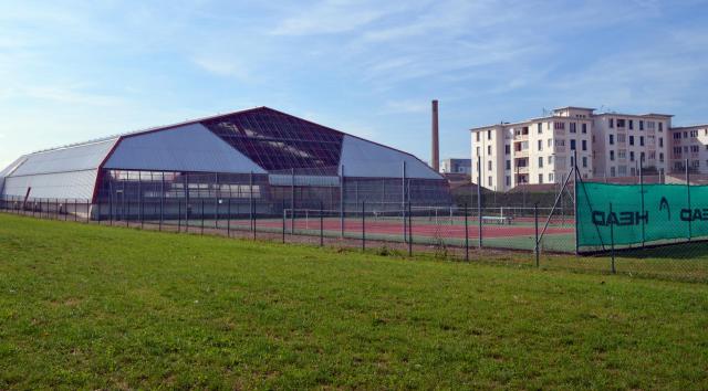 Bâtiment des courts de tennis couverts de Saint-Maurice-de-Beynost. On aperçoit derrière les bâtiments d'habitation de la Cité de la Soie…