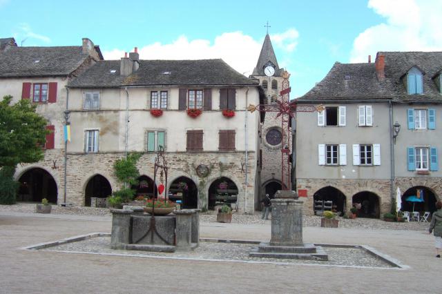 Vue partielle du côté est de la place de Sauveterre-de-Rouergue, avec croix et clocher.